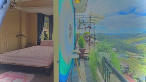A bedroom with a bed, a small table, and a balcony with a view of a green landscape. - My Stay 1 Le Van Tam (Xuan Huong - Da Lat)