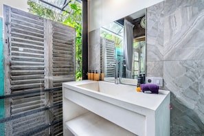 A bathroom with a large mirror, a white sink, and a marble wall. - Your Dream Waterfront Villa  (Kediri)