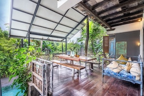An outdoor patio with wooden furniture, a pool, and lush greenery. - Your Dream Waterfront Villa  (Kediri)