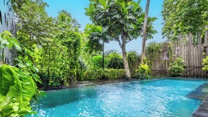 Une piscine entourée d’une végétation luxuriante et délimitée par une clôture en bois.