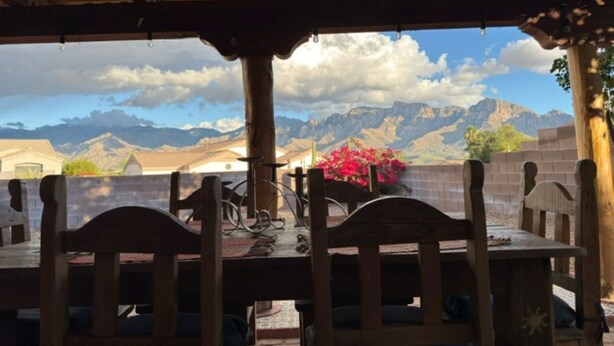 Una mesa y sillas de madera bajo un porche cubierto, con vistas a la montaña.
