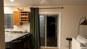 Una cocina con barra, un portón corredizo de vidrio que da a una habitación oscura y un sofá gris.