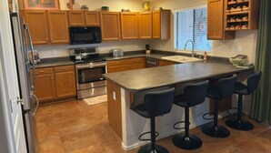 Una cocina con armarios de madera, un refrigerador de acero inoxidable, un microondas, un horno, un lavamanos y una zona de bar con taburetes.