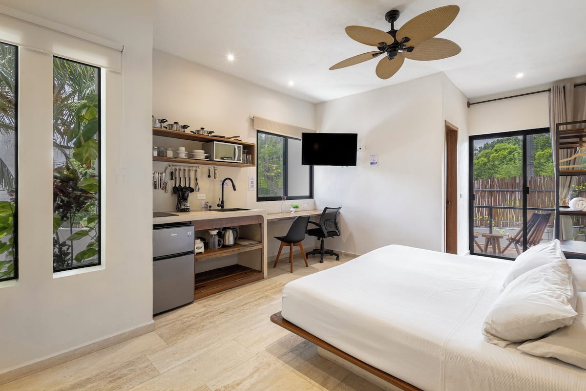 A modern bedroom with a bed, desk, and kitchenette.