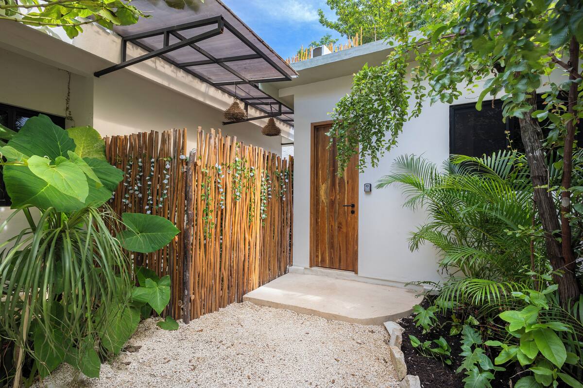 A modern house with a wooden fence, a concrete pathway, and lush greenery.