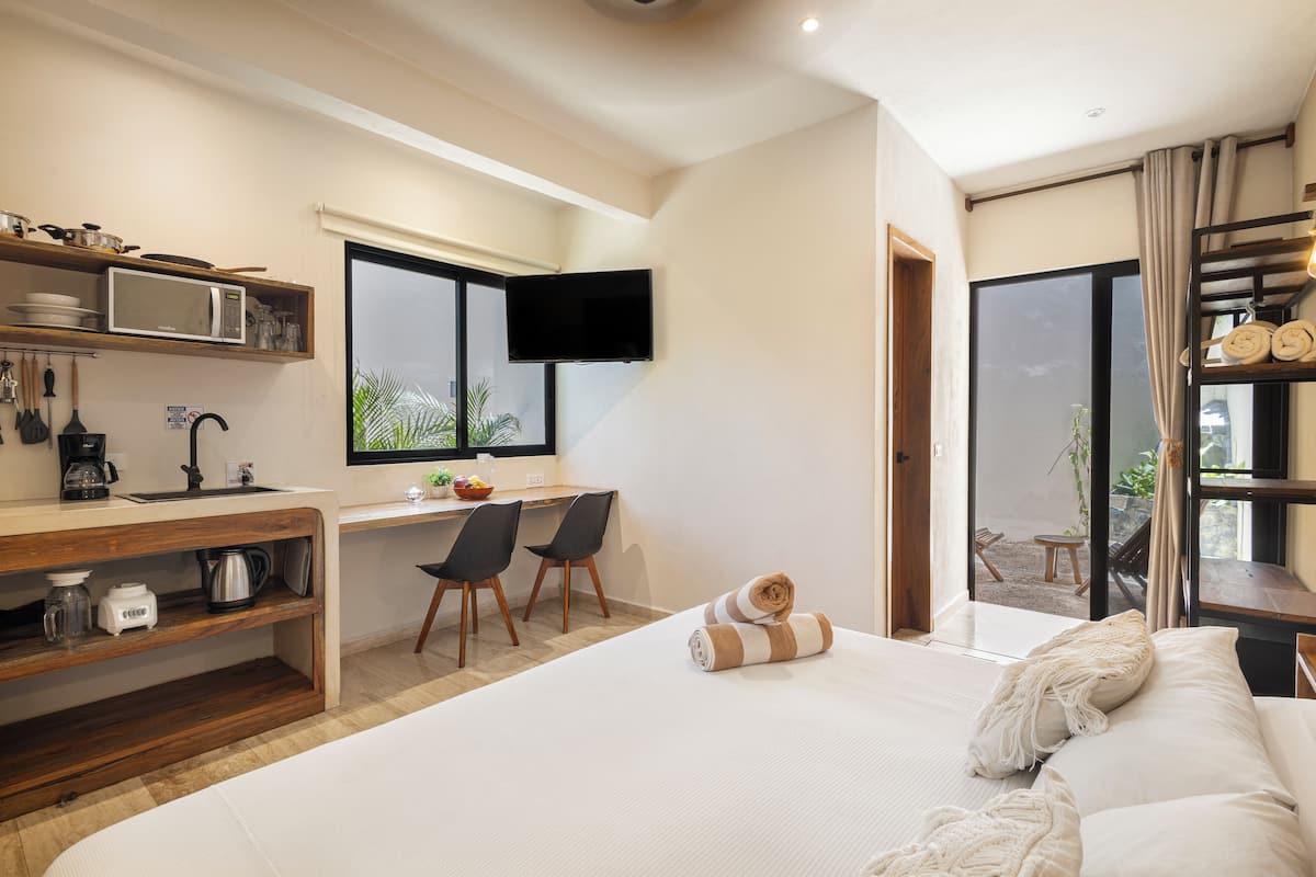 A modern hotel room with a large bed, a desk with two chairs, a flat-screen TV, and a balcony with a view.