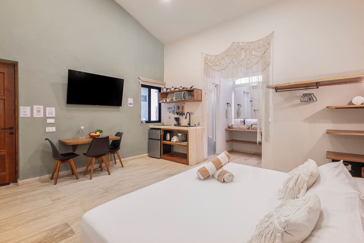 A modern hotel room with a bed, a desk, and a kitchenette.