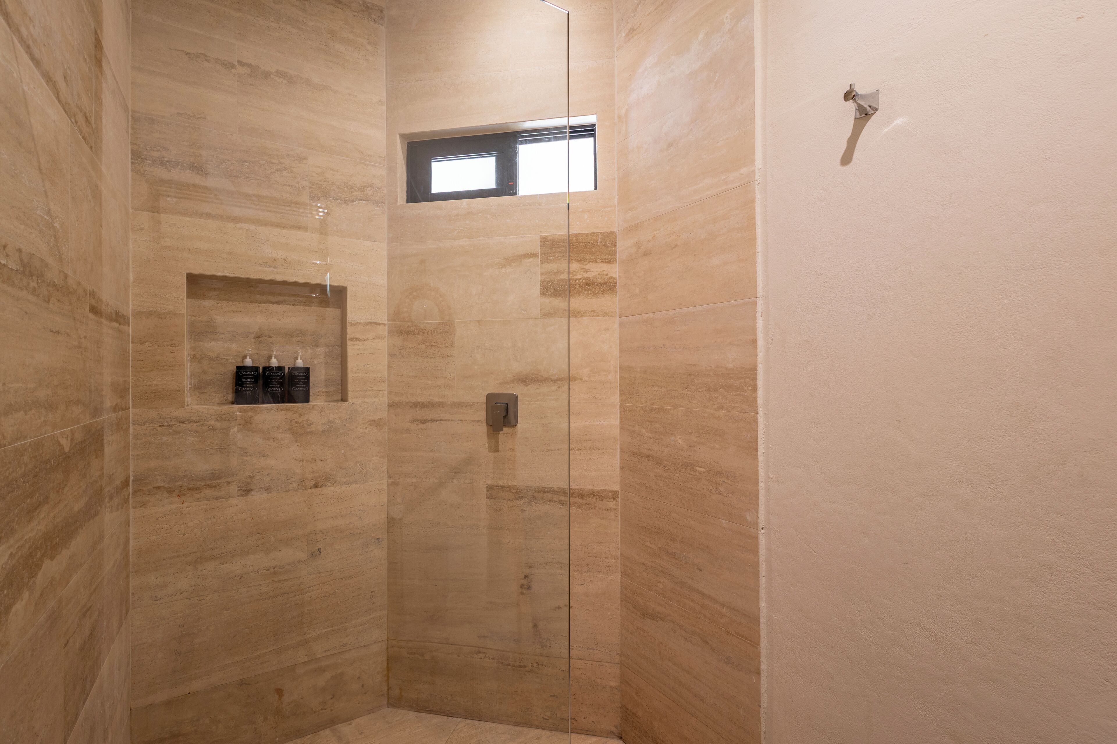 A modern shower area with a glass door, a small window, and a shelf with toiletries.
