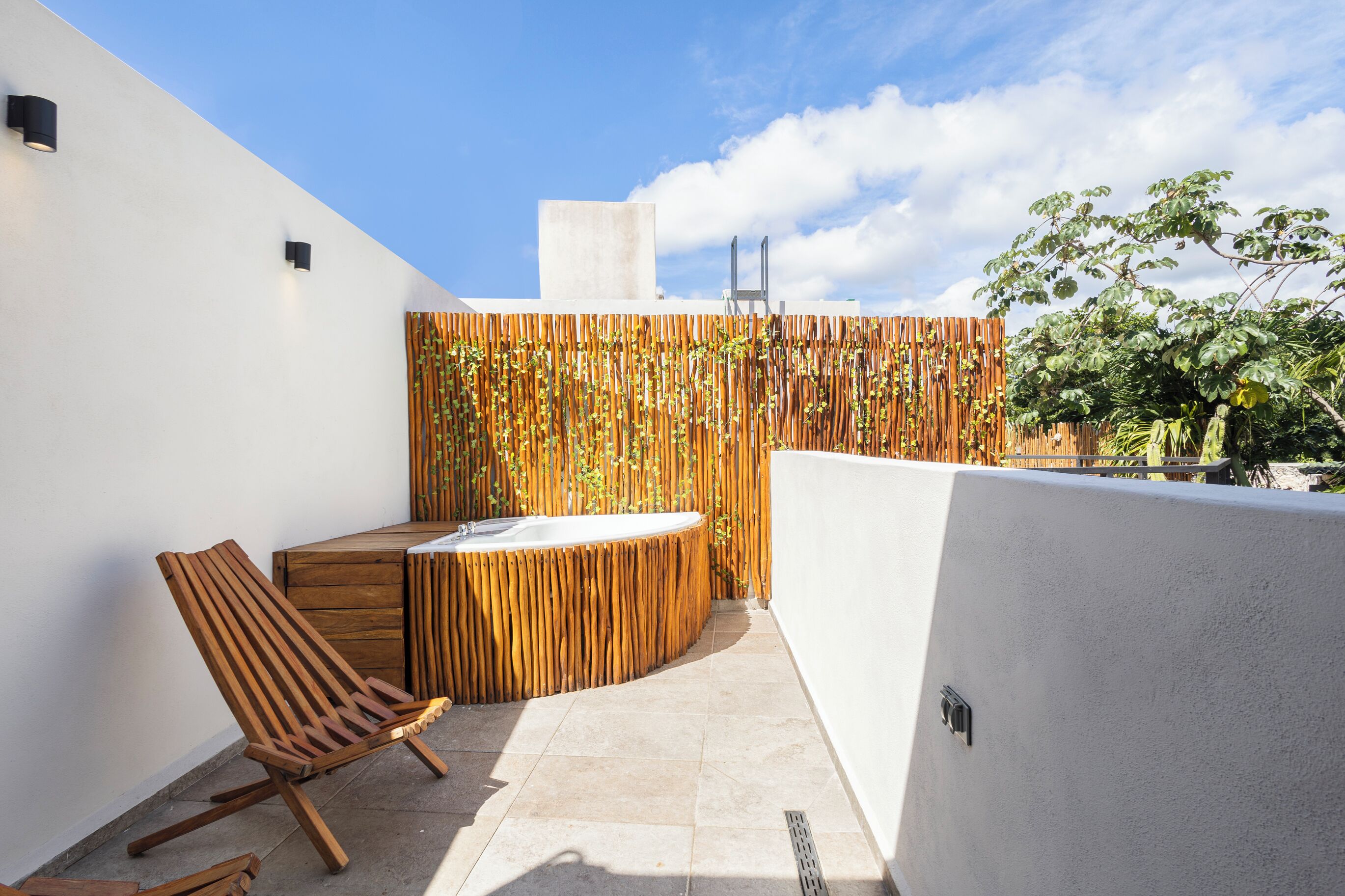 A modern outdoor patio with a wooden chair, a small wooden table, and a built-in hot tub.
