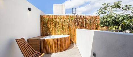 A modern outdoor patio with a wooden chair, a small wooden table, and a built-in hot tub.