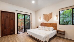A bedroom with a wooden bed, a sliding glass door to a patio, and a wall-mounted light fixture. - Casa Wayra Tulum - Boutique Condos (Tulum)