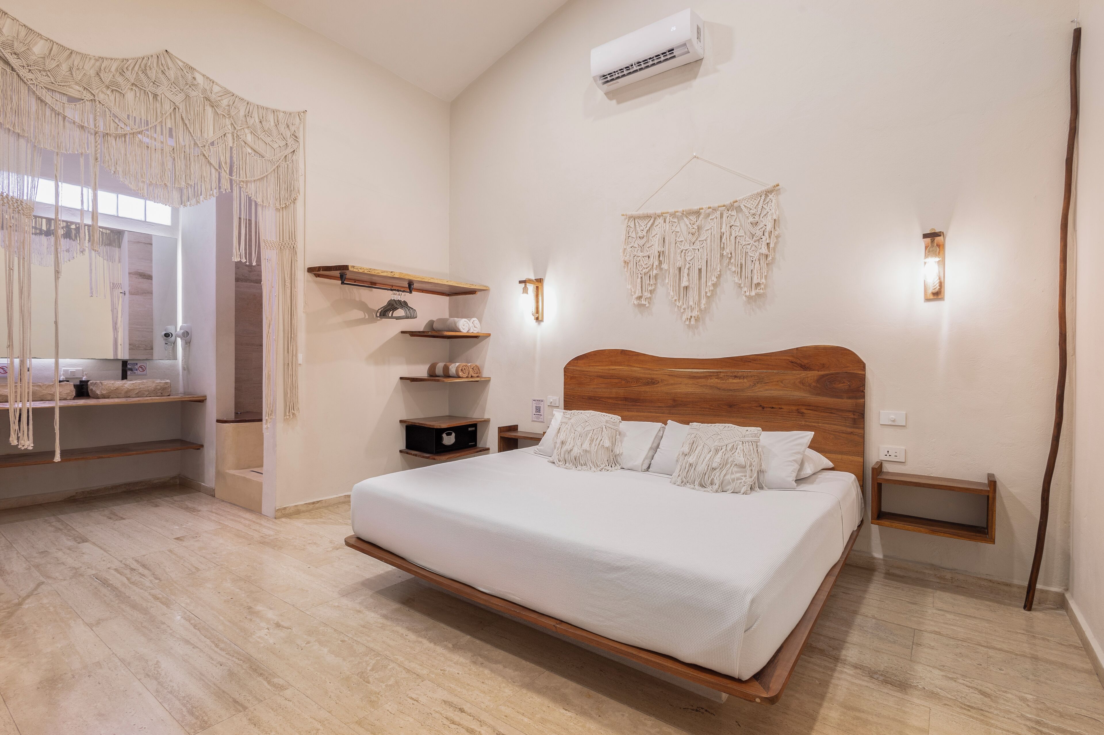 A bedroom with a wooden bed, white bedding, macramé wall hangings, and built-in shelves.
