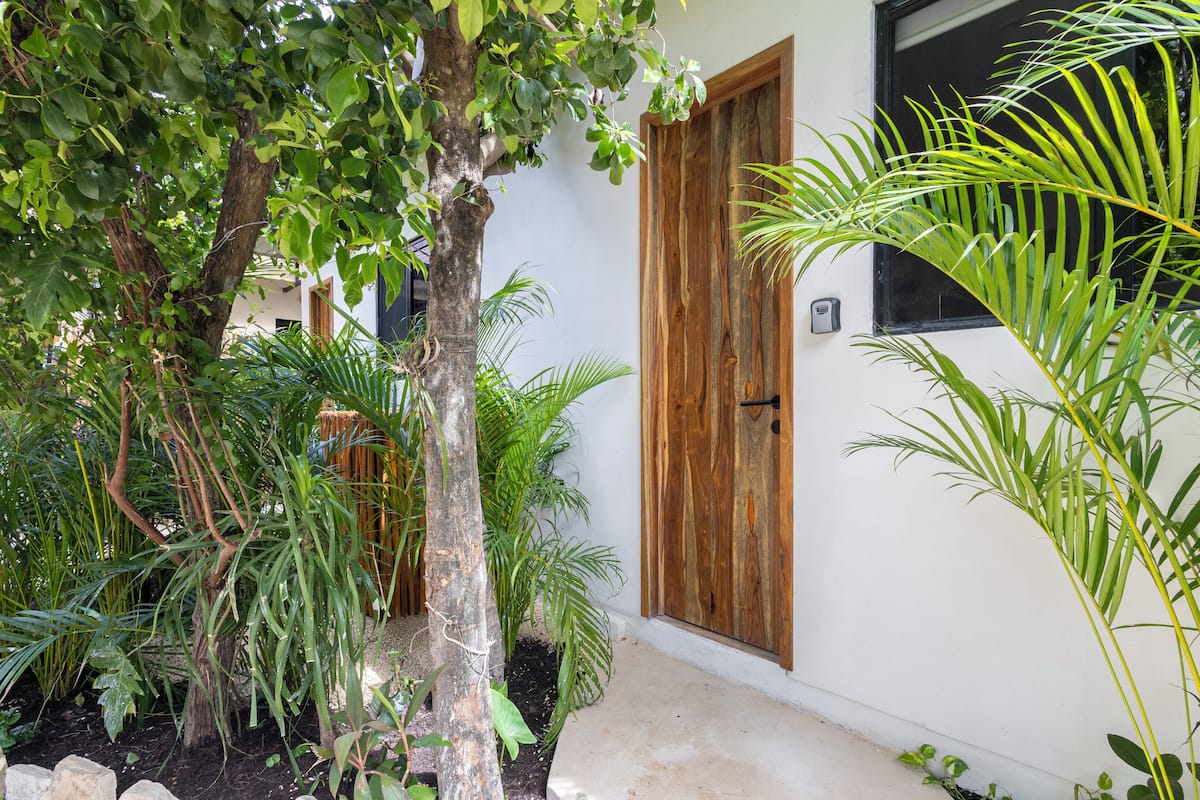 A building with a wooden door and a window, surrounded by various plants.