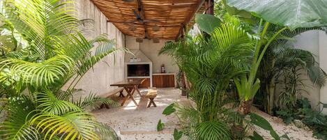 Un espacio al aire libre cubierto con una mesa y sillas, rodeado de diversas plantas tropicales.