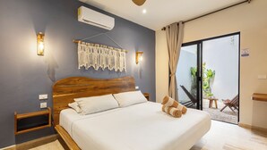 A bedroom with a wooden headboard, a bed with white linens, a wall-mounted air conditioner, and a sliding glass door leading to an outdoor area with chairs and a table. - Casa Wayra Tulum - Boutique Condos (Tulum)