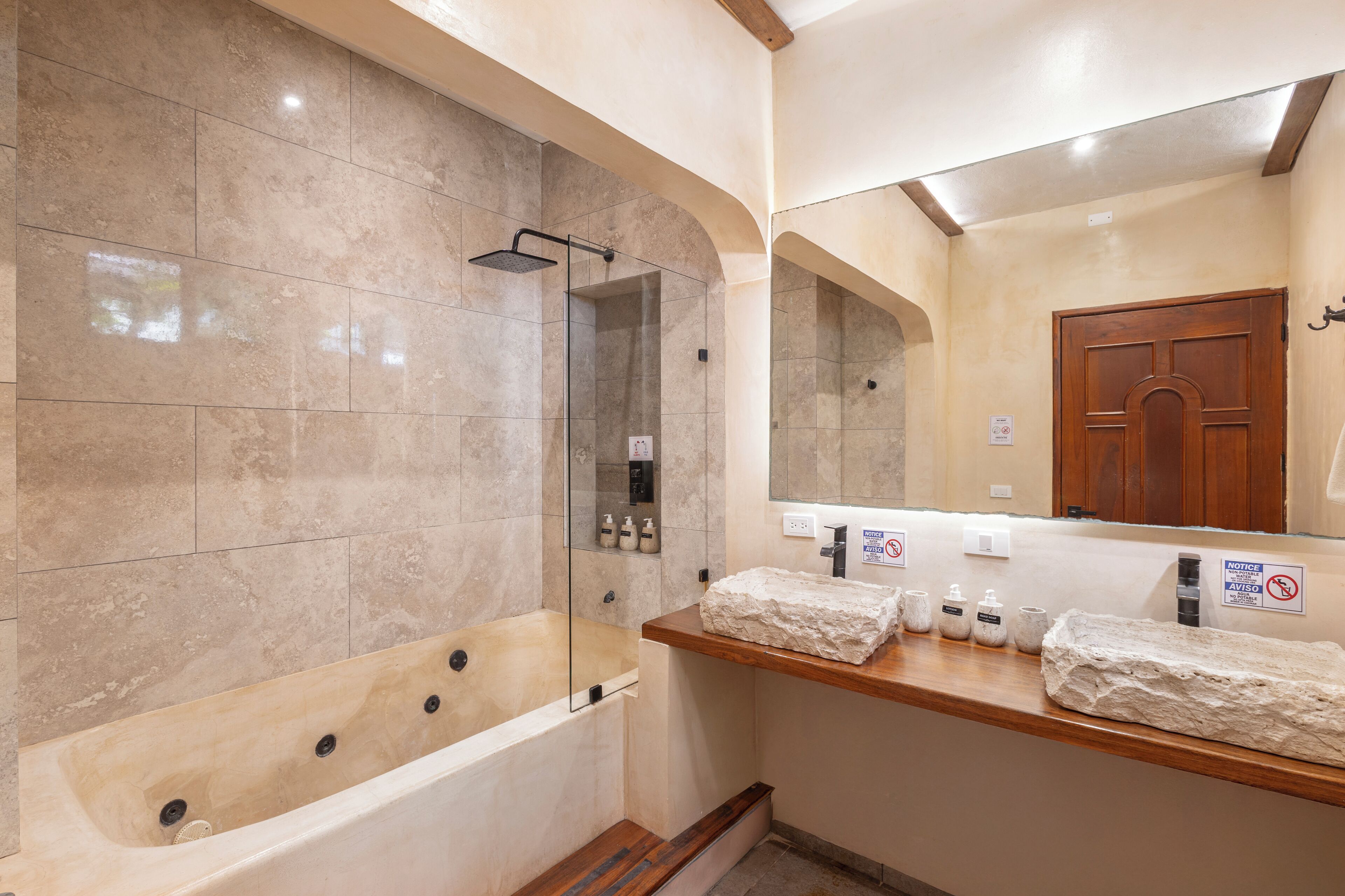 A bathroom with a bathtub, a glass-enclosed shower, and a wooden vanity with toiletries.