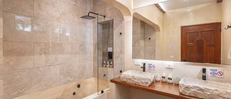 A bathroom with a bathtub, a glass-enclosed shower, and a wooden vanity with toiletries.
