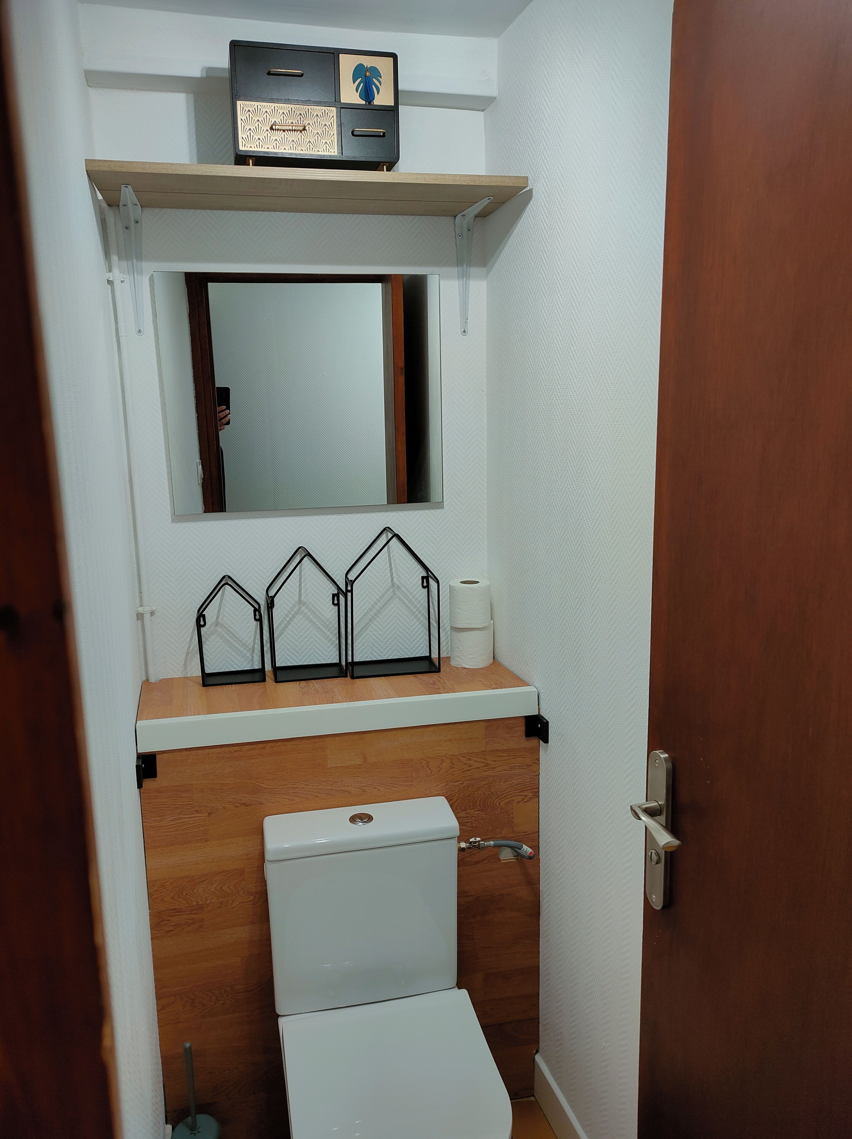 Een kleine badkamer met toilet, een spiegel en een plank met decoratieve objecten.