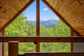 Ein dreieckiger Holzrahmen für ein Fenster mit Blick auf eine bewaldete Bergkette.