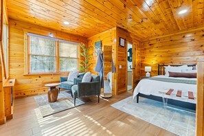 Ein Holzhütten-Interieur mit einem Bett, einer Couch, einem Tisch und einem Fenster.