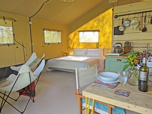 Ein gemütliches Schlafzimmer mit einem Bett, einem Sessel, einem Tisch mit einer Flasche und einer Küchenzeile mit Kochgeschirr.