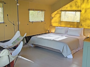 Ein Schlafzimmer mit einem Bett, Nachttischen, einem Sessel und Fenstern.