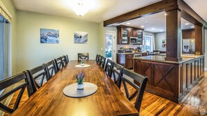 A spacious dining area with a long wooden table and chairs, a kitchen with dark wooden cabinets and stainless steel appliances, and a view of the outdoors. - Spacious, Modern 4BR house with city view and easy access to ski resorts (Salt Lake City)