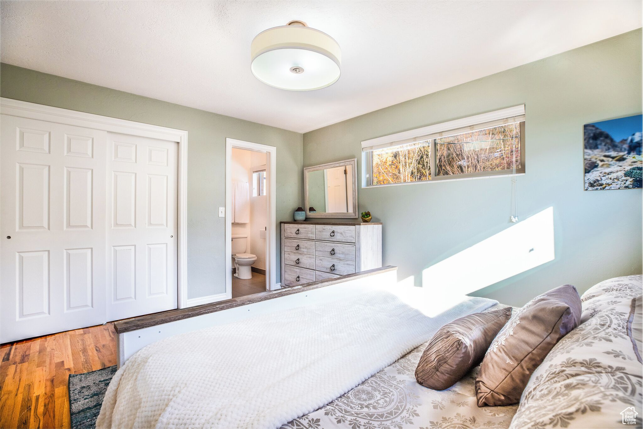 A bedroom with a bed, a dresser, a mirror, and a window with a view.