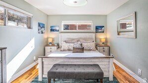 A bedroom with a large bed, bedside tables, a bench, and artwork on the walls. - Spacious, Modern 4BR house with city view and easy access to ski resorts (Salt Lake City)