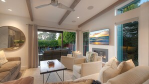 A modern living room with a fireplace, comfortable seating, and a large window with a view of the outdoors. - Luxury 3-Bed Beach Cottage with Hot Tub, Fire Pit, BBQ - Walk To Beach (Cardiff By The Sea)