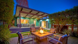 A patio area with a fire pit and outdoor seating, surrounded by greenery and a house in the background. - Luxury 3-Bed Beach Cottage with Hot Tub, Fire Pit, BBQ - Walk To Beach (Cardiff By The Sea)