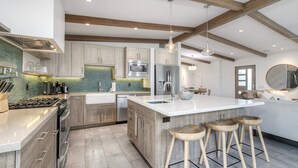 A modern kitchen with wooden cabinets, a large island with stools, stainless steel appliances, and a hanging light fixture. - Luxury 3-Bed Beach Cottage with Hot Tub, Fire Pit, BBQ - Walk To Beach (Cardiff By The Sea)