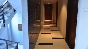 A modern hotel hallway with a staircase on the left, a tiled floor, and a wooden door at the end. - Annex Suites Bogura (Bogra)
