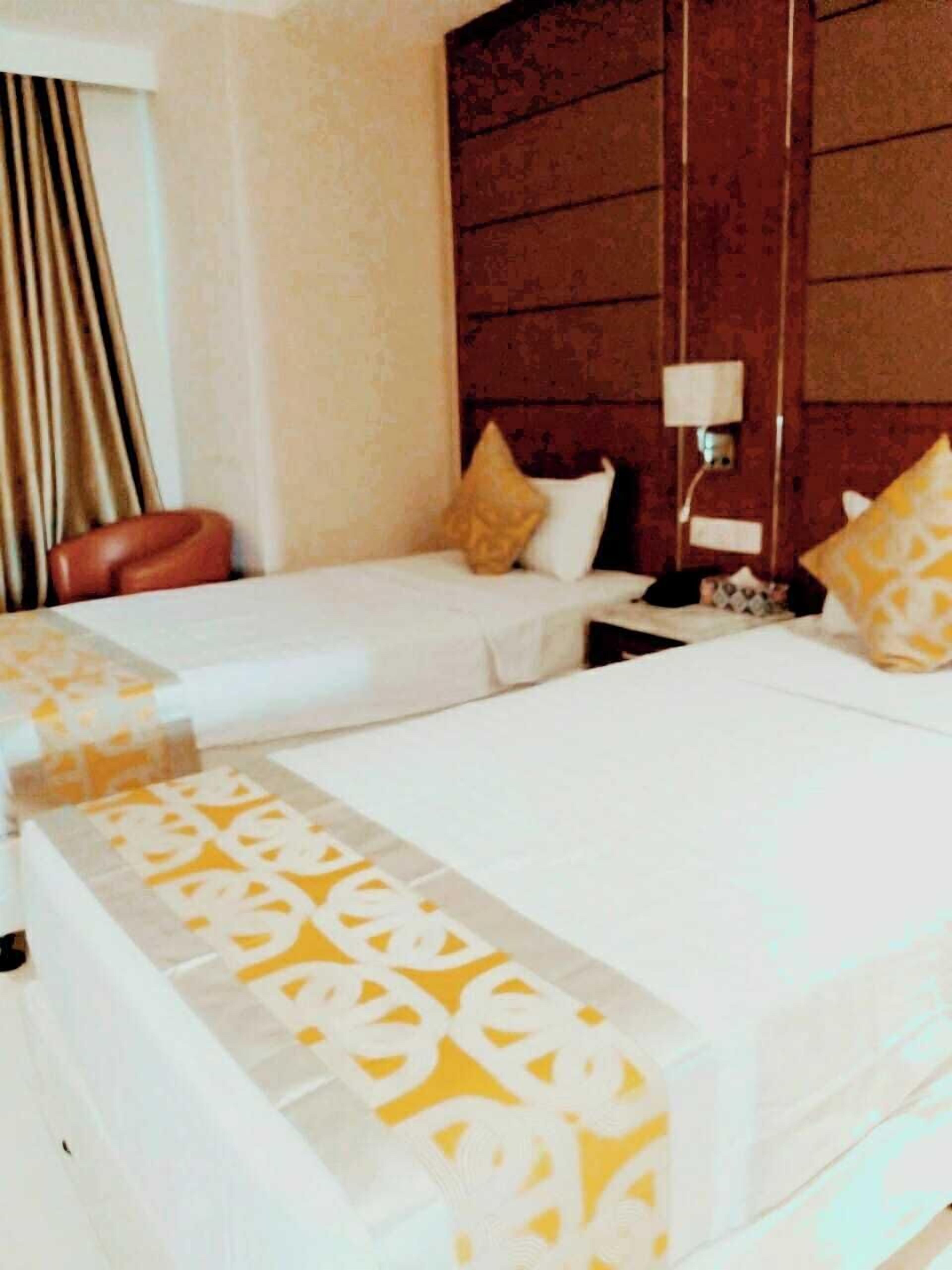 A hotel room with two beds, a wooden headboard, a nightstand, and a lamp.
