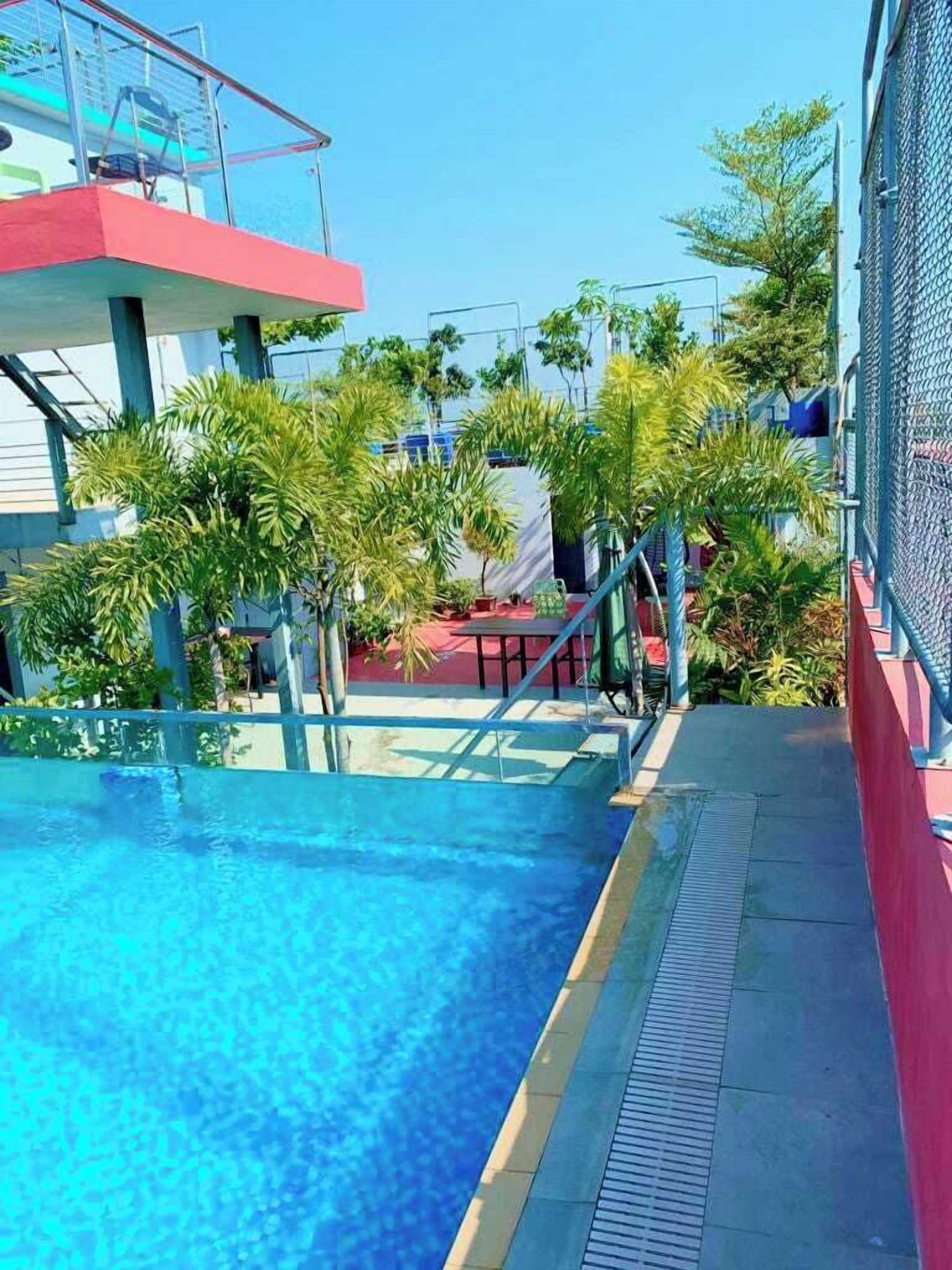 A swimming pool with a clear blue water surface, surrounded by palm trees and a red and white building structure.
