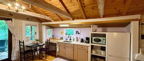 A cozy kitchen with wooden beams, a dining area with a table and chairs, and a refrigerator.