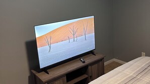 Ett sovrum med en TV på ett träställ, en säng med ett randigt överkast och en grå vägg.
