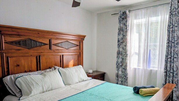 Een slaapkamer met een houten hoofdeinde, een bed met een blauwgroene sprei en een nachtkastje met een lamp.