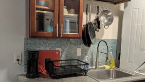 Een keuken met houten kastjes, een RVS vaatwasser, een granieten aanrechtblad, een koffiezetapparaat en een spoelbak met afwasmiddel.