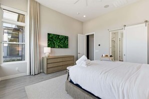A modern bedroom with a large bed, a wooden dresser, a green leafy wall art, and a sliding door closet. - Sierra Vista - Gated Community in Sereno Canyon (Scottsdale)