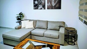 Ein modernes Wohnzimmer mit einem grauen Ecksofa, einem Glastisch und zwei gerahmten Fotografien an der Wand.