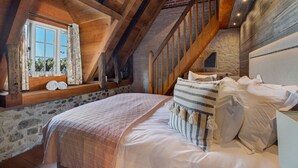 Un dormitorio acogedor en el ático con techo de madera, pared de piedra y una cama grande con ropa de cama blanca.