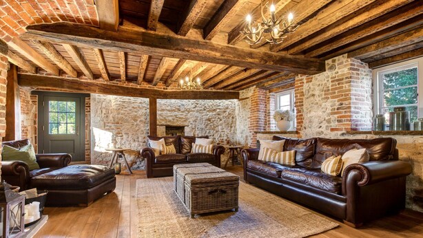 Una sala de estar rústica con vigas de madera a la vista, paredes de piedra, sofás de cuero y una chimenea.
