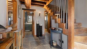 Una escalera de madera con una lámpara moderna, un suelo de piedra y vistas a una habitación con un armario y un espejo.