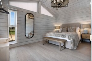 A bedroom with a large bed, a bench, a mirror, and a nightstand with a lamp.