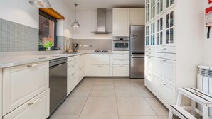 Een moderne keuken met witte kasten, roestvrijstalen apparatuur en hangende lampen.