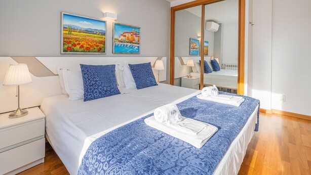Een hotelkamer met een groot bed, twee nachtkastjes, een spiegel en twee aan de muur bevestigde schilderijen.