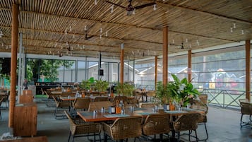 An outdoor restaurant with bamboo ceiling, wicker furniture, and potted plants.