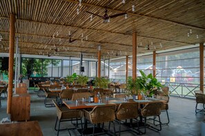 An outdoor restaurant with bamboo ceiling, wicker furniture, and potted plants. - Trishvam Palolem Beach Resort (Canacona)