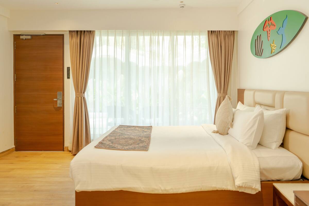 Ett hotellrum med en dörr av trä, en säng med vita sängkläder, en dekorativ matta och ett konstverk på väggen.